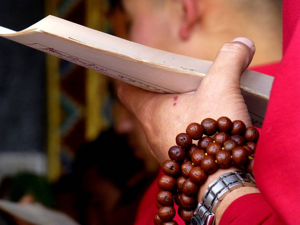 Una mano di un monaco buddista in preghiera con sacre scritture e perline religiose durante una cerimonia in un monastero a Sikkim, India. - Foto, immagini
