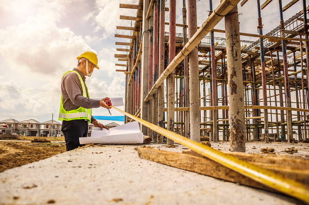 Aasian liikemies rakennusinsinööri työntekijä suojakypärä ja piirustukset paperi käsillä mitata betonilattia talon rakennustyömaalla - Valokuva, kuva