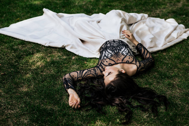 Kaunis viehättävä nainen musta valkoinen mekko ja katso pois. Nuori nainen makaa vihreällä ruoholla - Valokuva, kuva