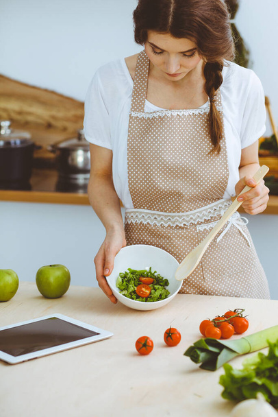 Young brunette woman cooking in kitchen. Housewife holding wooden spoon in her hand. Food and health concept - Foto, afbeelding