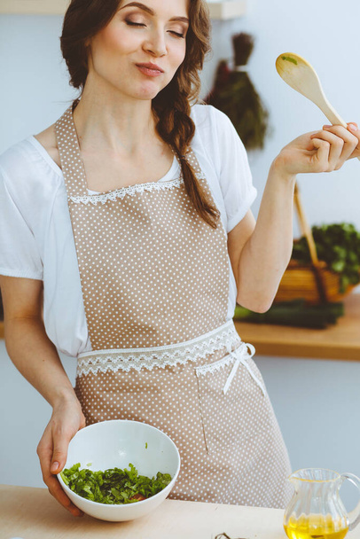 Young brunette woman cooking in kitchen. Housewife holding wooden spoon in her hand. Food and health concept - Fotografie, Obrázek