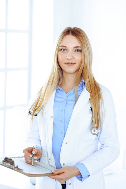 Young woman doctor at work in hospital office. Blue color blouse of therapist looks good. Medicine and healthcare concept - Zdjęcie, obraz