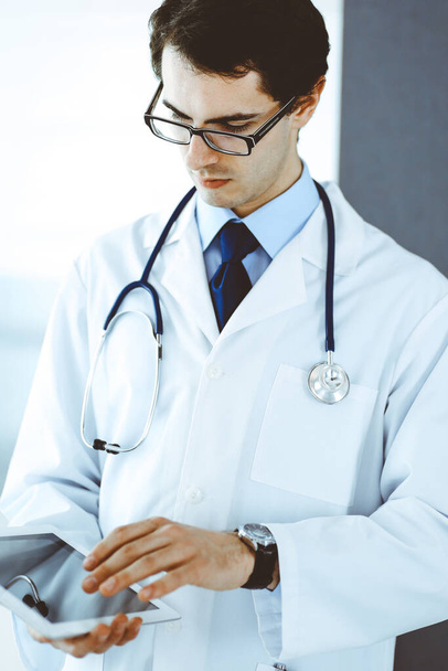 Doctor man using tablet computer for network research or virtual disease treatment. Perfect medical service in clinic. Modern medicine, medic data and healthcare concepts - 写真・画像