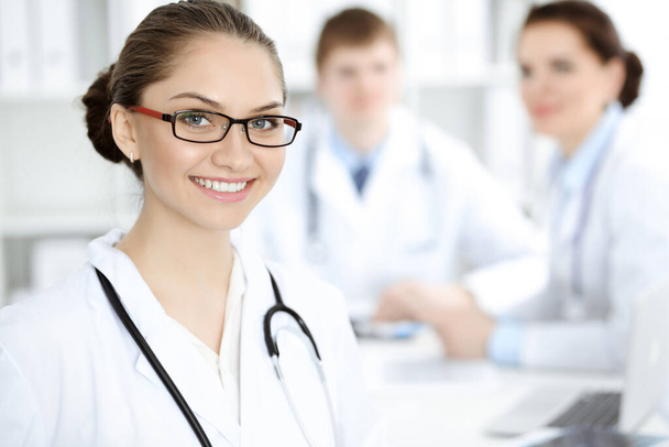 Happy smiling woman-doctor sitting and looking at camera at meeting with medical staff . Medicine concept - Foto, afbeelding