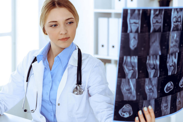 Doctor woman examining x-ray picture near window in hospital. Surgeon or orthopedist at work. Medicine and healthcare concept. Blue colored blouse of a therapist looks good - Foto, Imagen