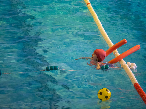 Niña aprendiendo a nadar con un flotador en clase de natación en una piscina cubierta - Foto, Imagen