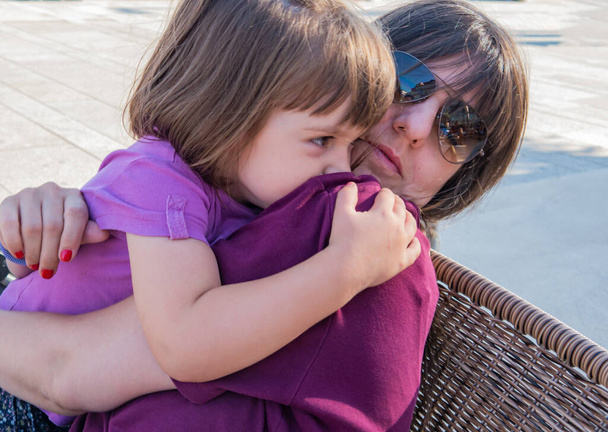 4歳の女の子抱擁彼女の母親しっかりとながら、彼女は路上でウィッカーチェアに座って - 写真・画像