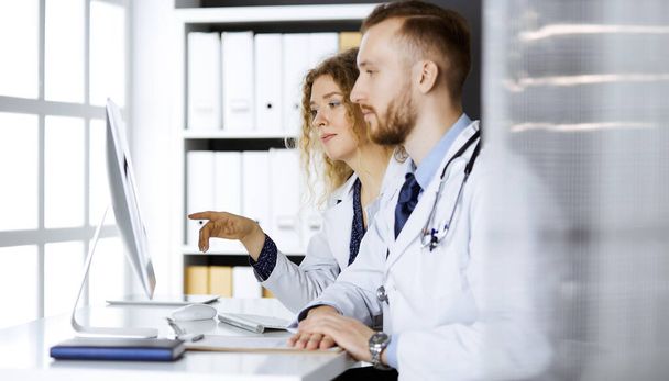 Red-bearded doctor with female colleague discussing current disease therapy while sitting at working place in clinic. Team work in medicine - Foto, Imagem
