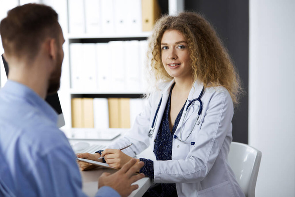 Female doctor and male patient discussing current health examination while sitting in clinic. Perfect medical service and medicine concept - Photo, image