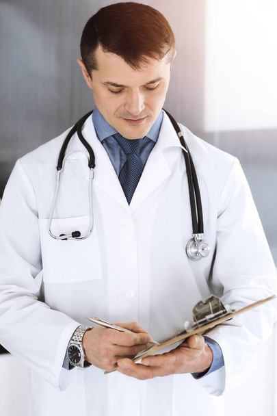 Doctor man using clipboard for filling up medication history records. Perfect medical service in clinic. Physician at work in hospital. Medicine and healthcare concepts - Photo, image