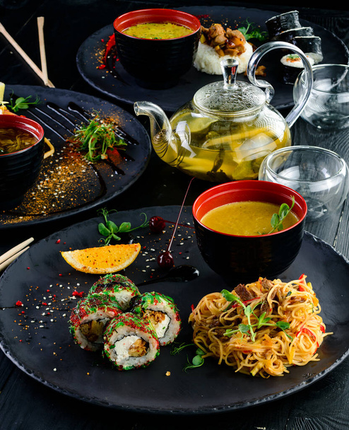 Traditional Japanese food - sushi, rolls, rice and udon noodles on a dark background. Top view of Asian food served table large set. Chinese, japanese and vietnamese cuisine - Фото, изображение