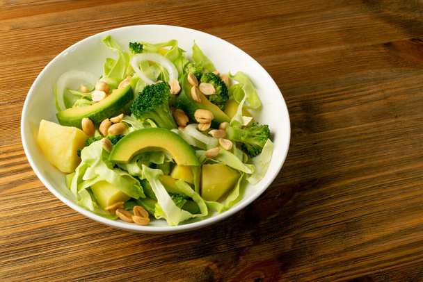 Zöld saláta avokádóval, uborkával, brokkolival, burgonyával és mogyoróval, fehér éttermi tányéron. Egészséges vegetáriánus saláta szeletelt aligátorkörtével vagy avokádós körtével - Fotó, kép