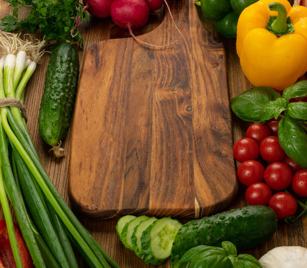 Cutting board vegetables mockup. Chopping board with fresh cucumbers, greens, peppers and cherry tomatoes ready for salad with copy space - Zdjęcie, obraz