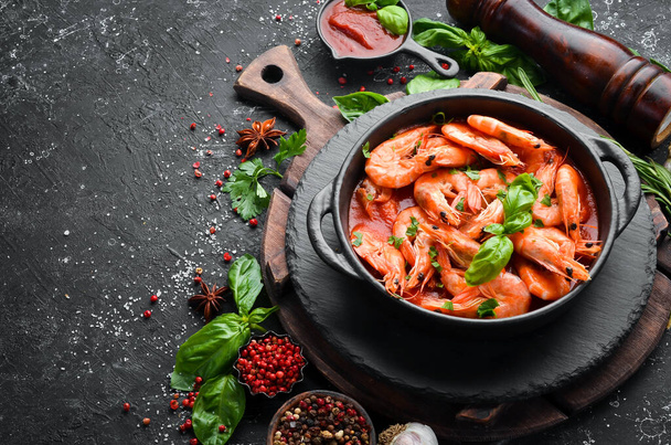 Food. Boiled shrimp in tomato sauce with basil on a black stone plate. Top view. Free space for your text. - Foto, afbeelding