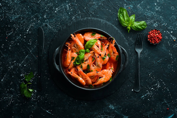 Eten. Gekookte garnalen in tomatensaus met basilicum op een zwarte stenen plaat. Bovenaanzicht. Vrije ruimte voor uw tekst. - Foto, afbeelding