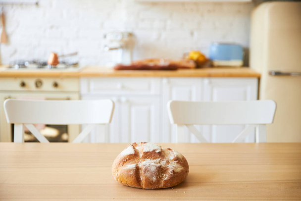 Fresh baked bread on a wooden table on the white kitchen is out of focus. - Photo, Image