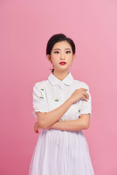 Nuori houkutteleva ja kaunis aasialainen nainen, jolla on kauniit kasvot, poseeraa ja hymyilee kameralle eristettynä vaaleanpunaisella taustalla - Valokuva, kuva