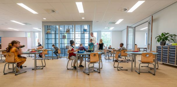 ARNHEM / NETHERLANDS - AUGUST 28 2020: Children in primary school work together in groups. They are located in a modern school building - Foto, immagini