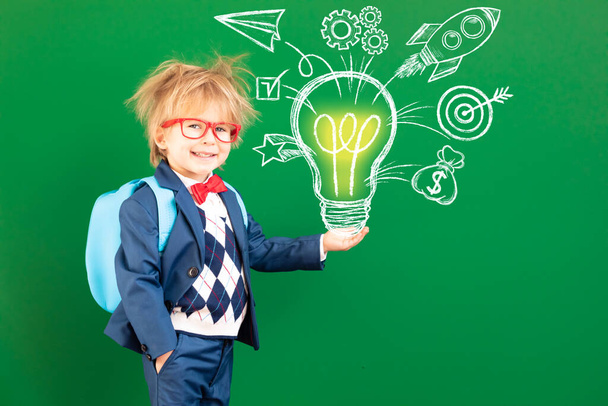 Bright idea! Funny child student with backpack in class. Happy kid against green chalkboard. Online education and e-learning concept. Back to school - Фото, зображення