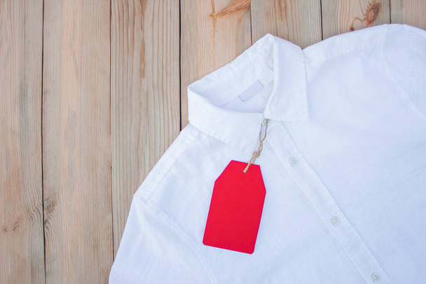 Червоний паперовий тег для одягу лежить на білій сорочці
 - Фото, зображення
