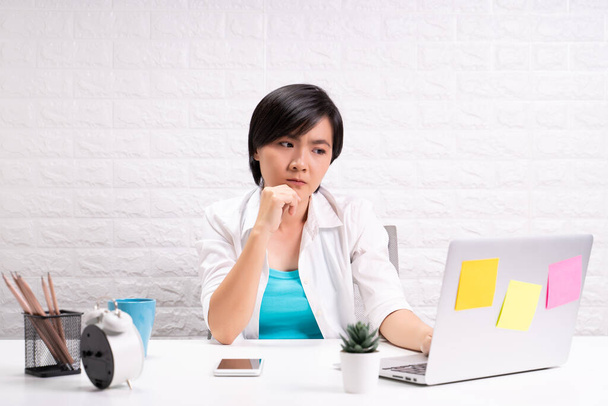 Przemyślana kobieta siedząca w biurze domowym pracująca za pomocą laptopa - Zdjęcie, obraz