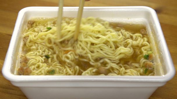 Az instant tésztát kínai evőpálcikával keverik. Sörfőtt sárga ramen speciális műanyag tányéron - Fotó, kép