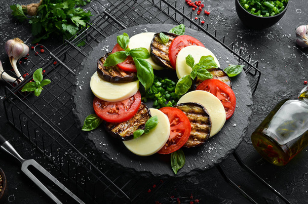 Caprese salad with basil. Tomatoes, mozzarella cheese and eggplant on a black stone plate. Top view. Free space for your text. - Foto, immagini
