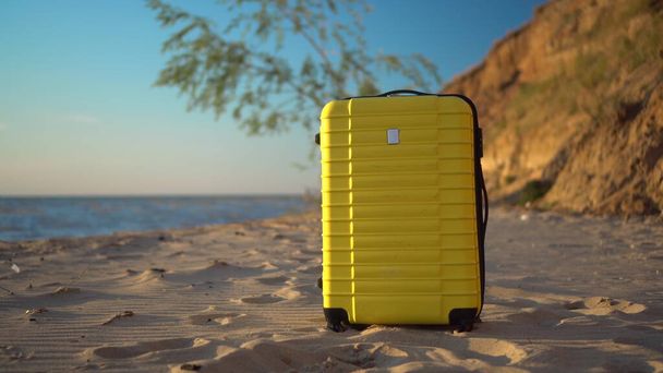 Жовта валіза стоїть на пляжі на тлі моря. Подорожі валіза
. - Фото, зображення
