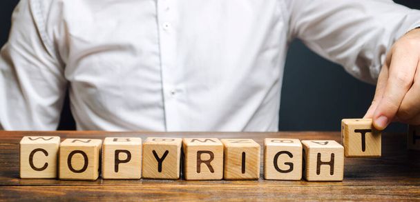 Businessman puts wooden blocks with the word Copyright. Patenting. Copyright protection. Brand and patent. The fight against online piracy. - 写真・画像