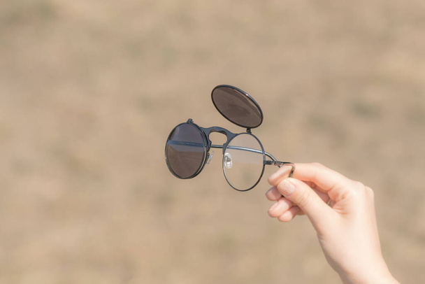 Steampunk-Sonnenbrille Modell in der Hand mit runden Gläsern Retro-Flip-Up-Modell Nahaufnahme an einem Sommertag gehalten. Selektiver Fokus - Foto, Bild