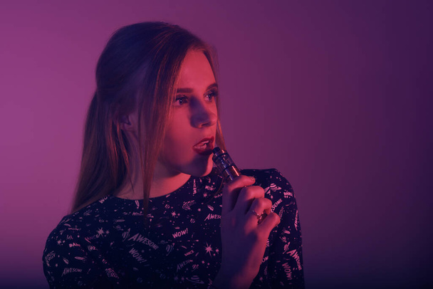 Girl vape in neon. A beautiful girl holds a vape in her hands and blows out smoke. - Φωτογραφία, εικόνα