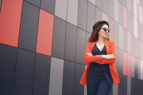Una ragazza con una giacca rossa autunnale va al lavoro o all'università. Modello in tuta sullo sfondo dell'edificio. Moda autunno - Foto, immagini