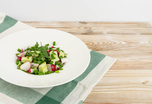 Voorjaarsradijssalade op houten achtergronden. Eenvoudige groene salade met gesneden radijsjes en komkommers - Foto, afbeelding