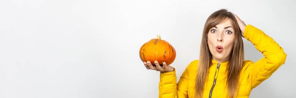 mladá dívka s překvapeným obličejem, držící dýňovou ruku, držící mu hlavu na lehkém pozadí. Halloween koncept, podzim, oslava. Nápis. - Fotografie, Obrázek
