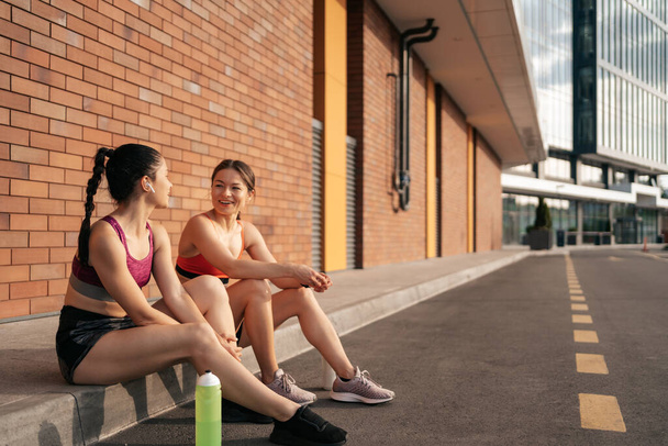 Портрет двух молодых красивых спортсменок отдыхающих после тренировки в городе - Фото, изображение