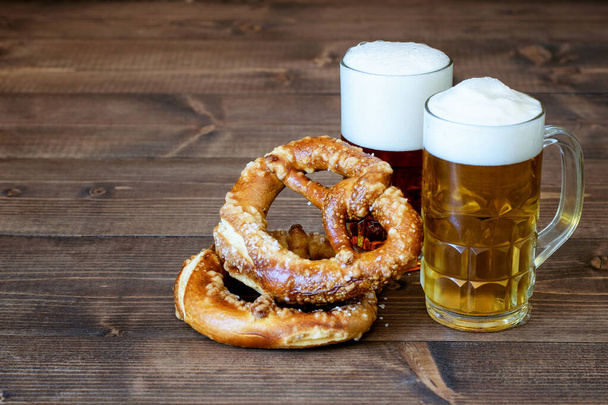 Tazas con cerveza clara y oscura, pretzels salados en el fondo de madera, perfecto para el festival de octubre.  - Foto, Imagen