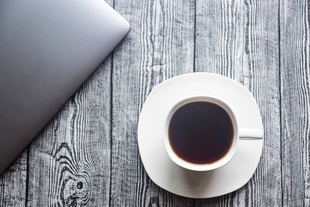 Кава в білій чашці на білій тарілці і ноутбук на сірому дерев'яному фоні
  - Фото, зображення