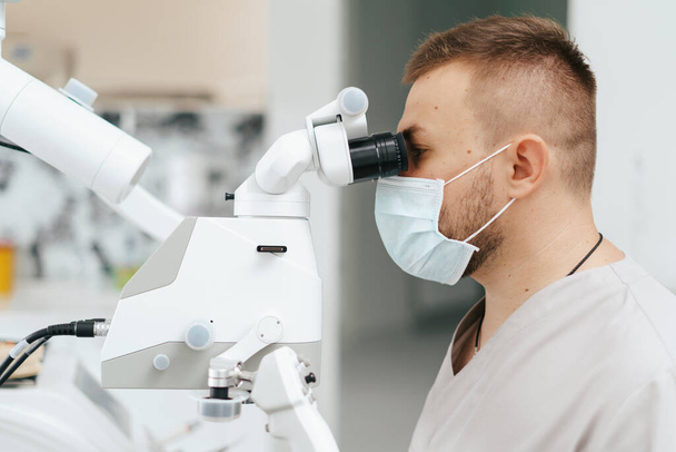 Dentiste masculin portant un masque regardant au microscope - Photo, image
