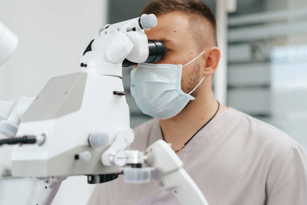Odontólogo masculino con máscara mirando al microscopio - Foto, imagen