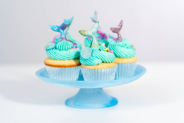 Gourmet-Meerjungfrau-Cupcakes mit blauem Buttercreme-Zuckerguss belegt und mit Streusel und Schokolade Meerjungfrauen-Schwänze dekoriert. - Foto, Bild