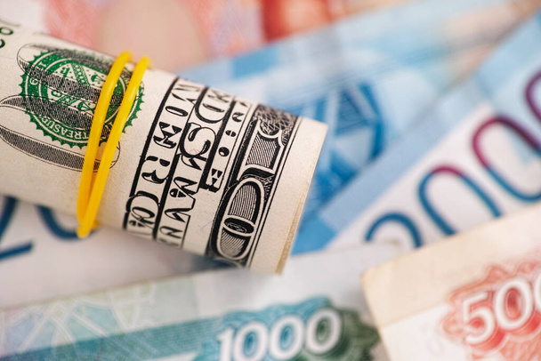 Rolled up american dollar bills on russian ruble banknotes. Close up. - 写真・画像