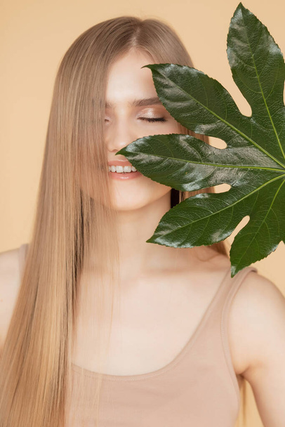 Έννοια φυσικών καλλυντικών για το δέρμα του προσώπου, τα φρύδια και τα μαλλιά. Πορτρέτο γυναίκα με πράσινο φύλλο, ξανθιά μοντέλο κορίτσι με χαμόγελο - Φωτογραφία, εικόνα