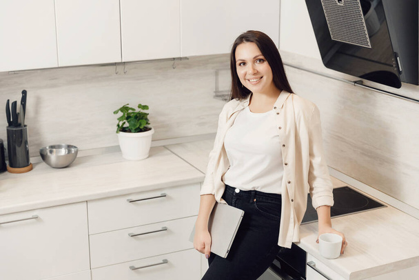 Mujer joven freelancer tiene portátil y café en casa de la cocina. Trabajo conceptual cuarentena en línea - Foto, Imagen