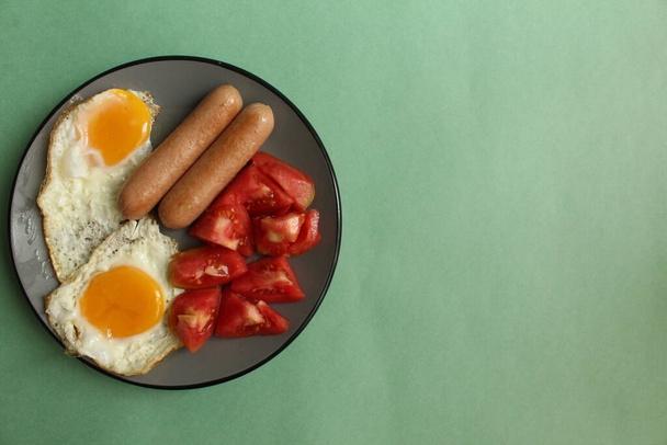 Reggeli élelmiszer szürke tányéron, zöld háttér kolbász paradicsom rántotta rántotta sült tojás másolási hely élelmiszer háttér - Fotó, kép