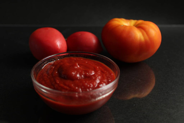 une casserole en verre avec sauce tomate rouge aux légumes se dresse sur un fond noir à côté de légumes tomates orange rouge et oignons dans une enveloppe jaune avec espace Kopi - Photo, image