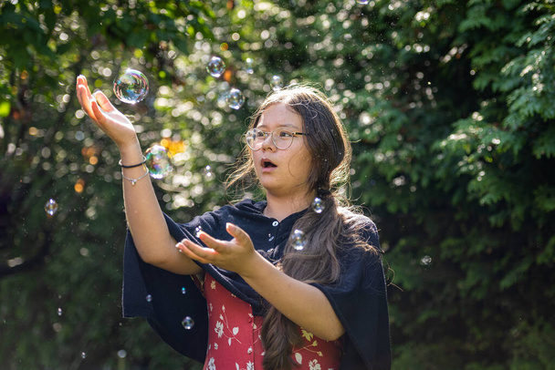 Een tiener die zeepbellen najaagt. Groene bladeren achtergrond - Foto, afbeelding