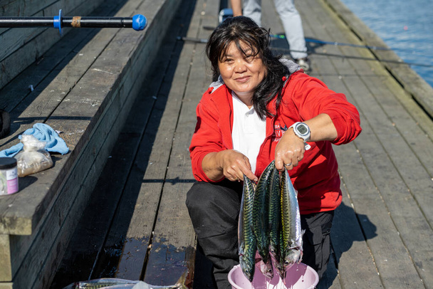 Улыбающаяся азиатка в свои 50 показывает свежий улов скумбрии - Фото, изображение