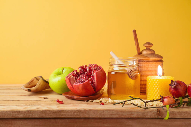 Jewish holiday Rosh Hashana concept with honey jar, apple and pomegranate on wooden table over yellow background - Zdjęcie, obraz