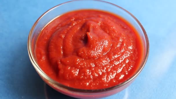 Salsa de tomate rojo en una cacerola de vidrio sobre un fondo azul sobre la comida - Imágenes, Vídeo
