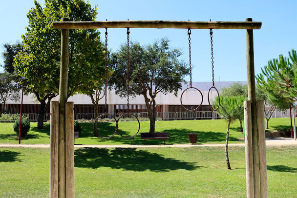 Металеві гімнастичні кільця різної довжини на дерев'яній опорі в зеленому міському парку
. - Фото, зображення